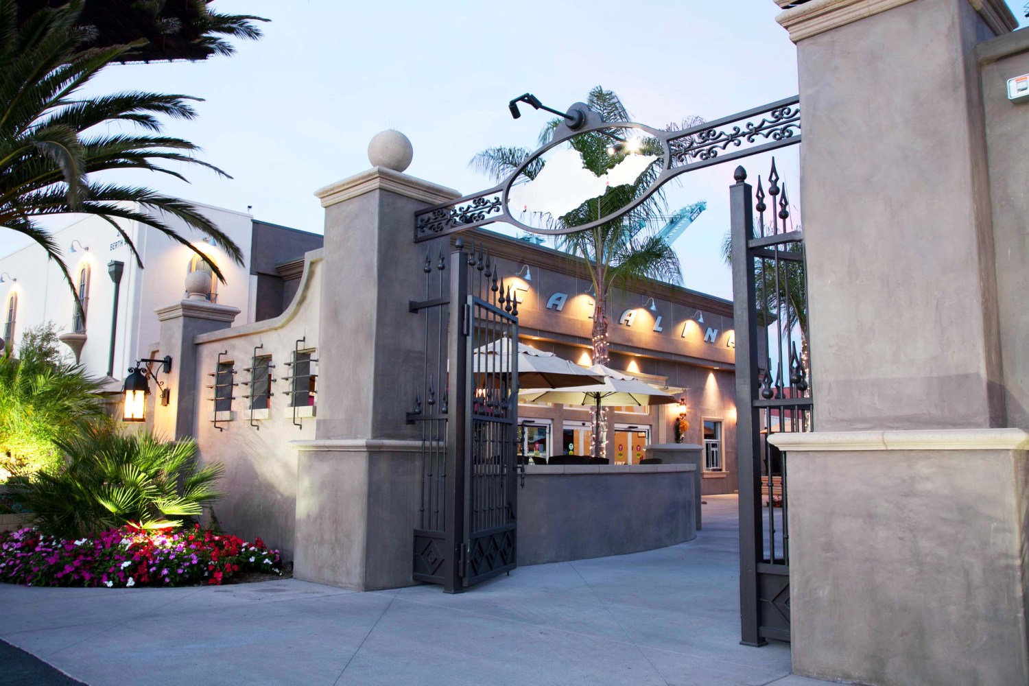 Elegant building entrance with open wrought iron gate, palm trees, and flowers.