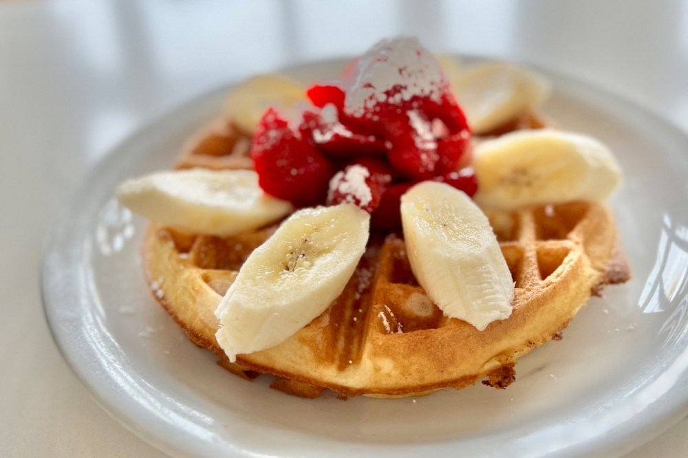 A plate of waffles with strawberries and bananas on top from the Pancake Cottage. 